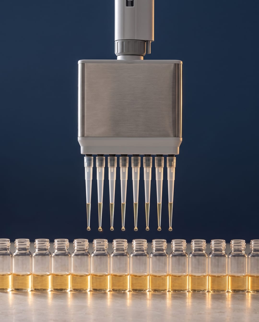 An eight-channel pipette lowering its tips over a row of small glass vials glowing in warm light.